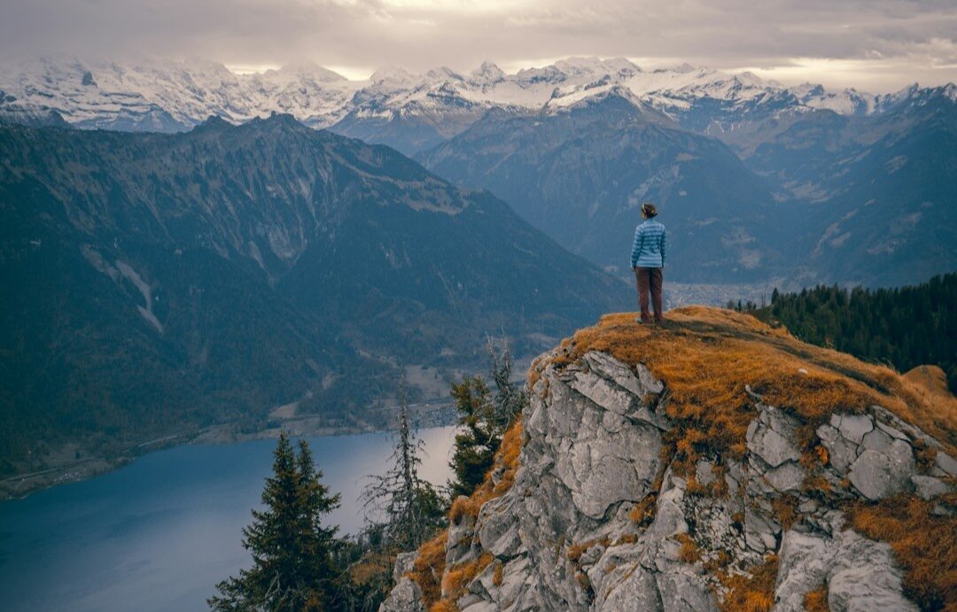 A person stands on top of a cliff looking out on a vast panoramic scene. Photo by Felipe Giacometti on Unsplash.