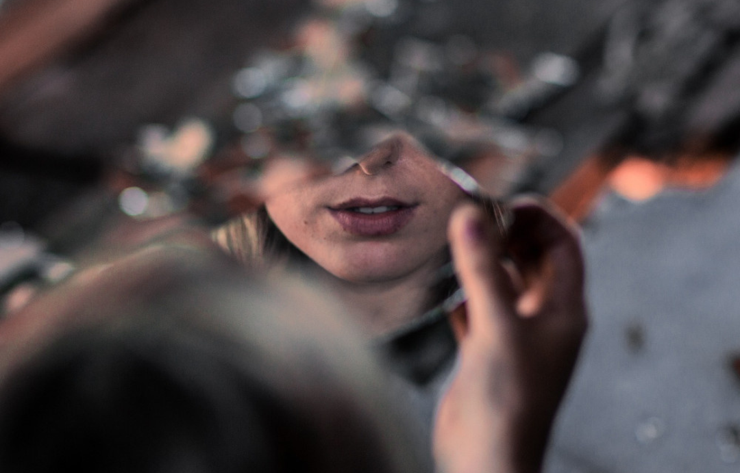 A woman looks into a broken mirror.