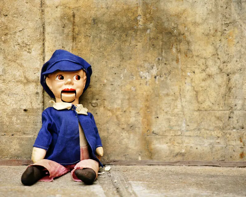 Ventriloquist dummy sitting against concrete wall. Photo by lisegagne, Canva Pro.